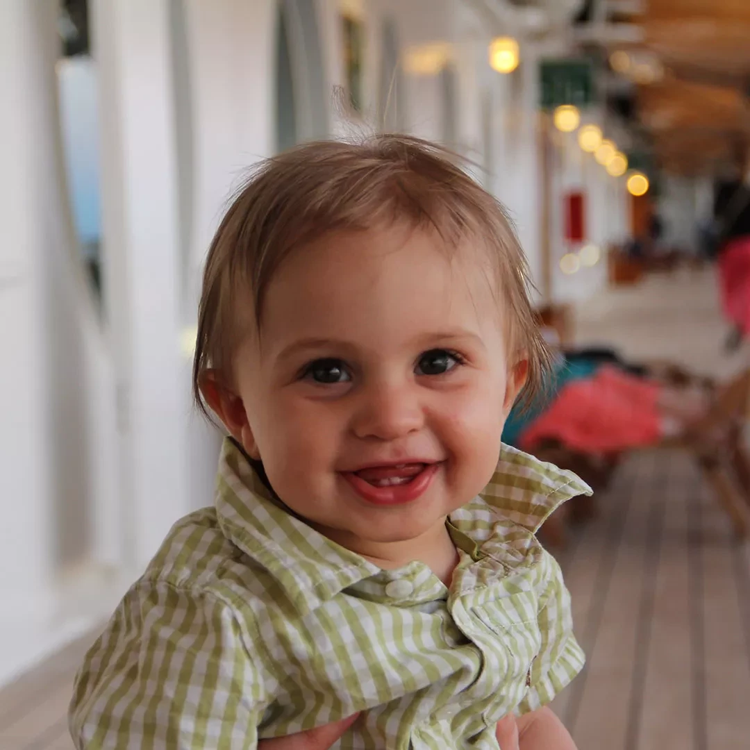 Smiling baby with tousled hair wearing a green checkered shirt.