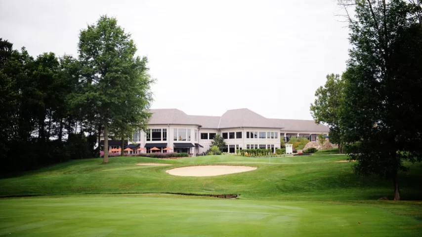 View of a golf course with a clubhouse in the background, surrounded by trees.