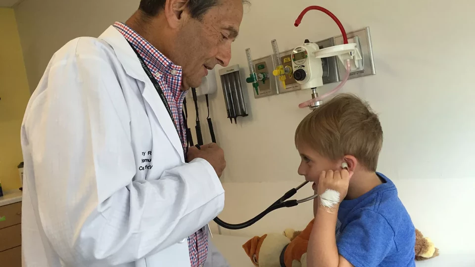 Doctor smiling as young boy listens to his heartbeat with a stethoscope.