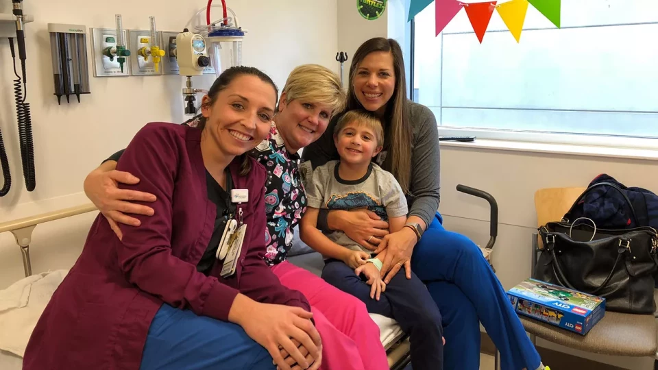 Smiling young boy surrounded by three women in a hospital room.